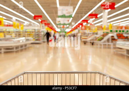 Blurred photos showcases shops on the background of a grocery cart. Long rows of racks with goods. Stock Photo