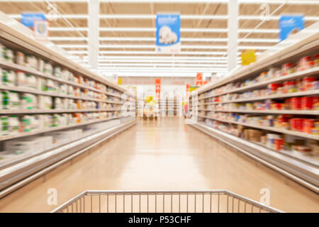 Blurred photos showcases shops on the background of a grocery cart. Long rows of racks with goods. Stock Photo