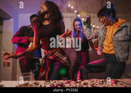 Friends dancing holding drinks at house party. Young women enjoying and having fun at the house party. Stock Photo