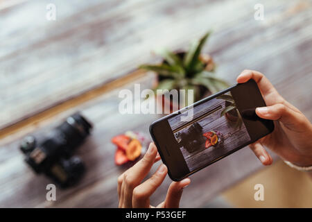 Close up of a woman taking photo of fruits in a bowl using a mobile phone for her food blog. Blogger capturing photo of a fruit bowl placed beside a c Stock Photo