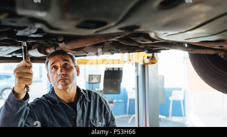 Experienced car mechanic repairing a lifted car in garage. Auto repair men fixing exhaust system of a car. Stock Photo
