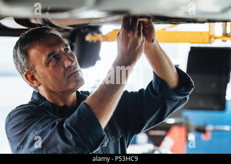 Car mechanic repairing a lifted car in garage. Auto repair men fixing a car in service station. Stock Photo