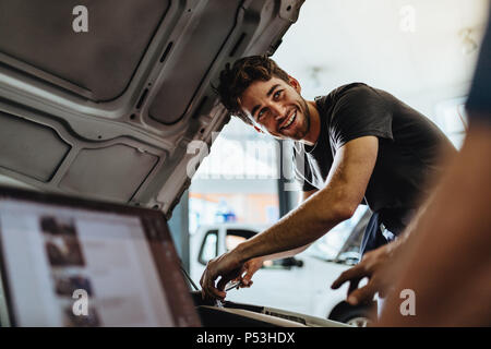 Auto mechanic fixing a vehicle in service station. Car mechanic working at automotive service center looking at his coworker and smiling. Stock Photo
