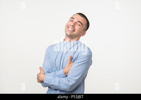 Attractive man in blue shirt laughs at funny story from friend with crossed hands and closed eye Stock Photo