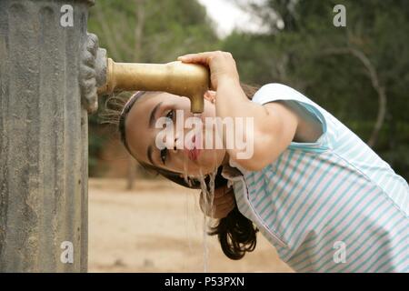 Niña de siete años bebiendo agua en una fuente. Stock Photo