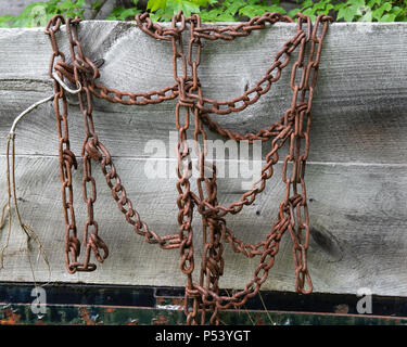 Old worn rusty tire chains for traction in snow and ice hanging on the wooden side on a truck in the Adirondack Mountains, NY USA Stock Photo