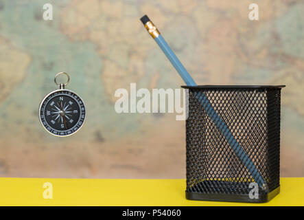 Compass and pencil in a metal pot on a blurred background of an old world map Stock Photo