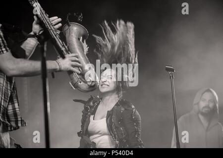 Singer (Echo) with standing hair on stage next to a saxophone while hooded musician watching in the background (Tito) Stock Photo