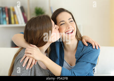 Happy girl kissing her friend sitting on a couch in the living room at home Stock Photo