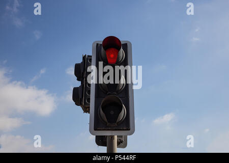 Red traffic light isolated warning the drivers to stop. Blue sky with clouds background. Closeup under view. Stock Photo