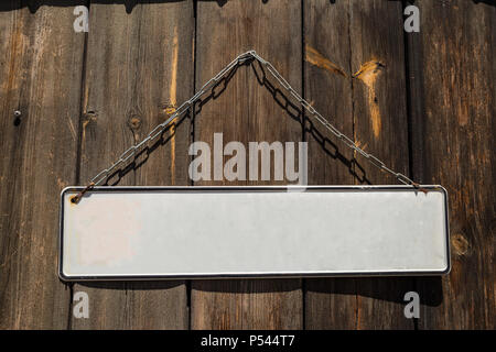 Wooden brown door with a white empty banner label hanging from metallic rusty chain in front of it. Closeup, space for text. Stock Photo