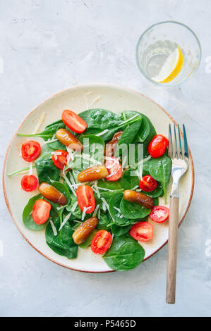 Fresh salad with spinach tomatoes and dates served on a plate. White stone background. Healthy eating concept. Stock Photo
