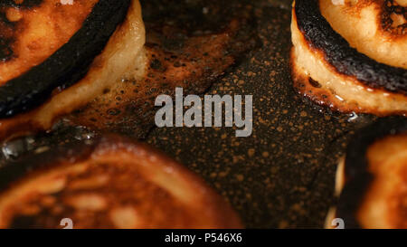 Closeup view burned pancakes frying in bubble vegetable oil on preheat cast iron pan at home. Stock Photo