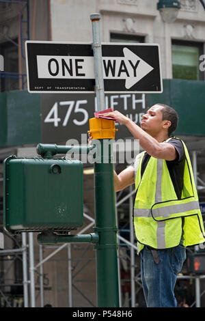 A young city worker on a ladder sands down a surface in preparation for repainting it. On Fifth Avenue in Midtown Manhattan, NYC Stock Photo