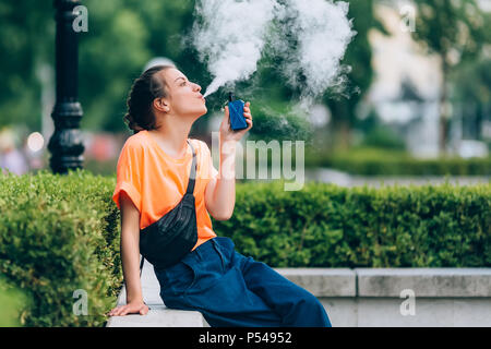 Pretty young girl vape popular ecig gadget,vaping device.Happy brunette vaper girl with e-cig.Portrait of smoker female model with electronic cigarett Stock Photo