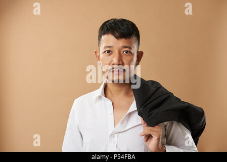 Young asian man office worker eith jacket on shoulder isolated on beige backgroundv Stock Photo