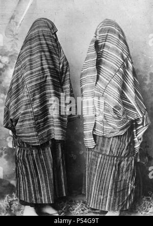 Scutari, Albania. Women in ordinary street costume of red and white cloth. The seams are joined with minute crochet and worked in red or color combinations. Under the skirt cloth which is tied like an apron around the waist are worn voluminous trousers on the Turkish style of black shiny cloth. August 1921 Stock Photo