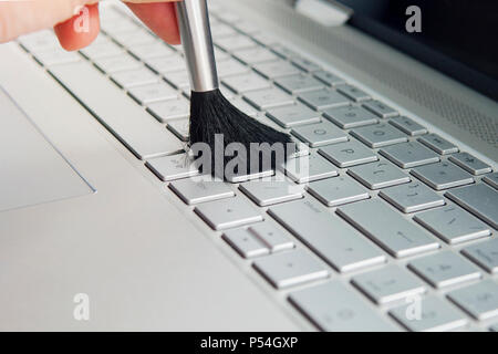 Cleaning keyboard and caring computer, cleaning the keyboard of the modern gray ultrabook transformer with a black brush from dust. Stock Photo