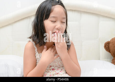 Cold And Flu. Little girl With Cough And Sore Throat Feeling Sick on bed. Closeup Of Unhealthy child In Scarf Coughing, Caught Cold. Health Care Conce Stock Photo