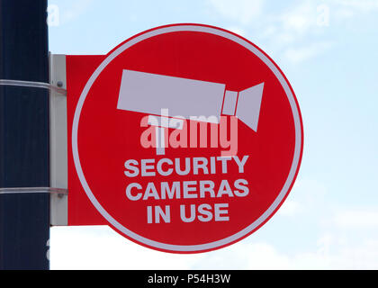 Red Security Cameras in Use sign on a pole with blue cloudy sky background. Warning would be criminals their actions will be recorded. Stock Photo