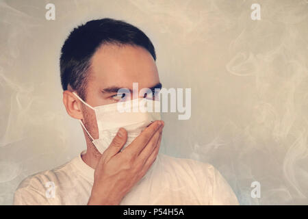 A young guy covers his nose in a mask. Bad smell the stench, the Concept of quarantine. smoke blanketing. the concept of air pollution and the environ Stock Photo