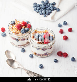 Two jars with tasty parfaits made of granola, berries and yogurt on white wooden table. Shot at angle. Stock Photo