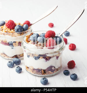 Two jars with tasty parfaits made of granola, berries and yogurt on white wooden table. Shot at angle. Stock Photo