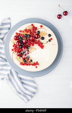 New York cheese cake with berries on white wooden table. Top view. Red currant, black currant and cherry. Stock Photo