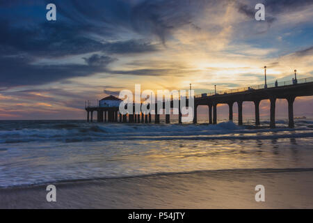 Long-exposure shot of colorful sky and clouds over Manhattan Beach Pier at sunset with smooth waves washing onto the beach, Manhattan Beach, Californi Stock Photo