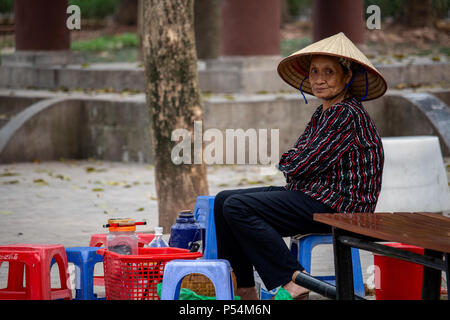 Hanoi, Vietnam - March 16, 2018: Local vietnamese woman sitting in her bar with small plastic chairs located in a park Stock Photo