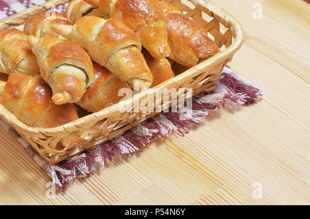 Wicker basket with home-made fresh croissants is on a napkin on a light wooden table. Stock Photo