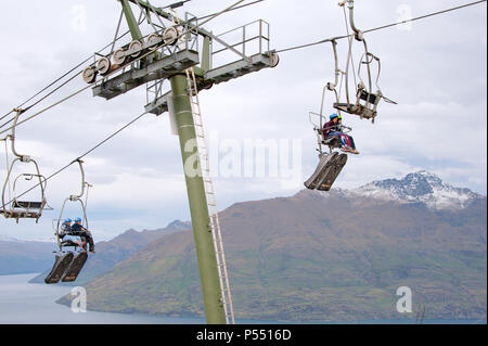 Queenstown, NZ – April 15, 2018: Fun riders with their carts on a cable chair lift going up the hill top for a luge ride with views of Lake and hills.