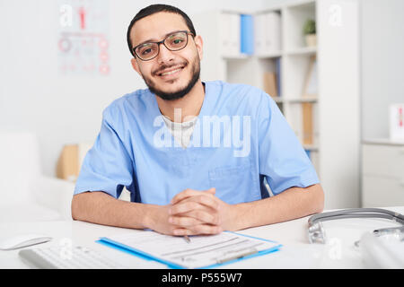 Smiling Middle-Eastern Doctor Posing at Desk Stock Photo
