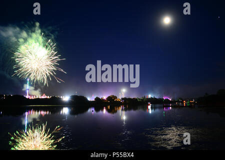 Newport, Isle of Wight, UK. 24th June, 2018. Fireworks and a near full moon herald the end of the last day of the Isle of Wight Festival as the Sunday night headliner band 'The Killers' play on the main stage, seen in the distance in blue lights. Photograph taken from the banks of the River Medina in Newport, Isle of Wight, June 24th 2018. Credit: Matthew Blythe/Alamy Live News Stock Photo