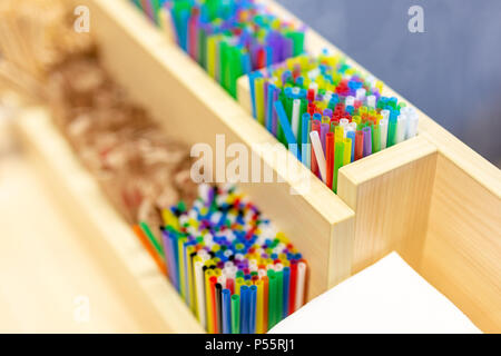 Bunch of colorful plastic sipping straws in wooden box at cafe counter. Drinks decoration and accessories. Bright multicolored background. Stock Photo