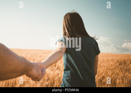 Rear view shot of young woman walking with her boyfriend on grass field. Couple enjoying a walk through grass land Stock Photo