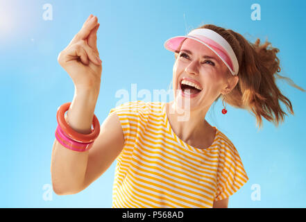 smiling young woman in yellow shirt against blue sky fingers snapping Stock Photo