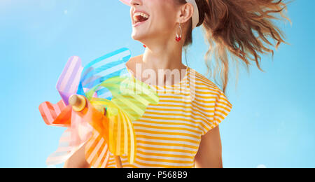 happy fit woman in yellow shirt against blue sky with colorful windmill looking into the distance Stock Photo