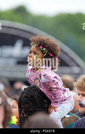 Gorgeous mixed race baby girl sitting on an adult's shoulders at the 2018 Africa Oye music festival in Sefton Park, Liverpool. Stock Photo