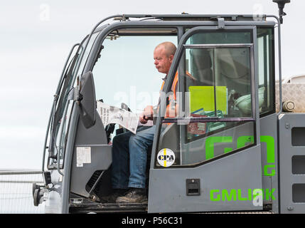 Workman sitting in construction vehicle reading a newspaper while taking a break from work, in the UK. Stock Photo