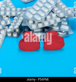 stack of different pills in a package and two red hearts on a blue background, copy space Stock Photo