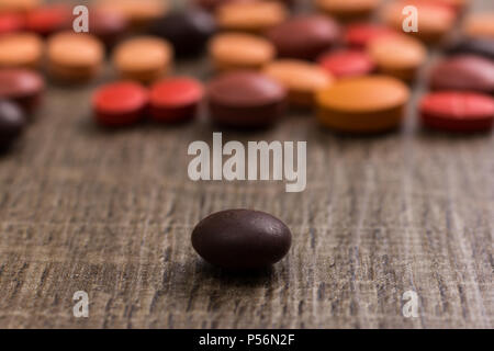 Heap of assorted orange, brown and red capsules on wooden table. One pill is apart, isolated. Stock Photo