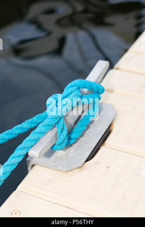 A cleat on a pier with a knotted blue rope Stock Photo