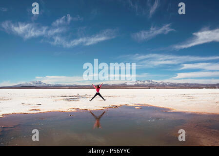 Happy jumping on the side of a natural salt puddle in Salar de Uyuni, Bolivia. Stock Photo