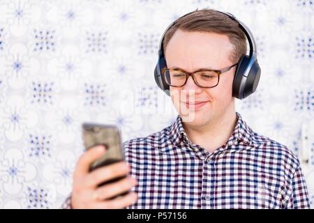 Young man with bluetooth headphones connected to smartphone in his hand Stock Photo