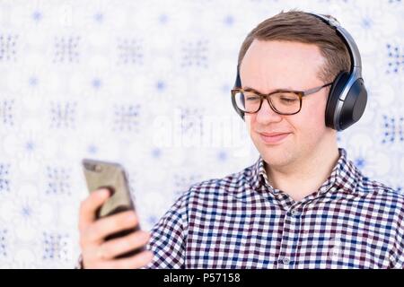 Young man with bluetooth headphones connected to smartphone in his hand Stock Photo