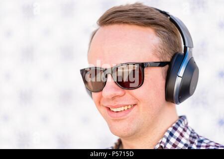 Young man listens something nice and smiles using the earphones. Stock Photo