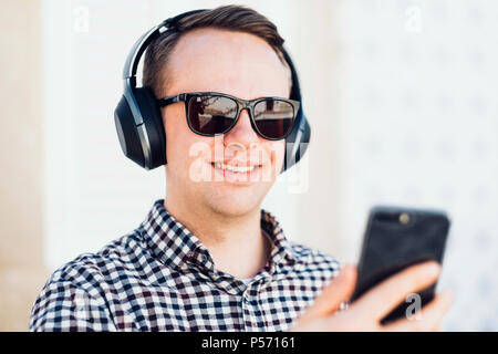 Young man with modern, good quality headphones enjoying the music from his smartphone Stock Photo