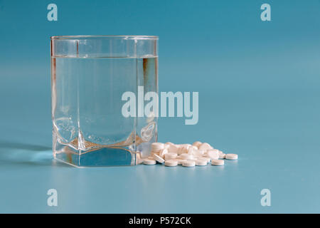 White pills and glass of water on the blue background. Glass of water and pills on blue background. Stock Photo