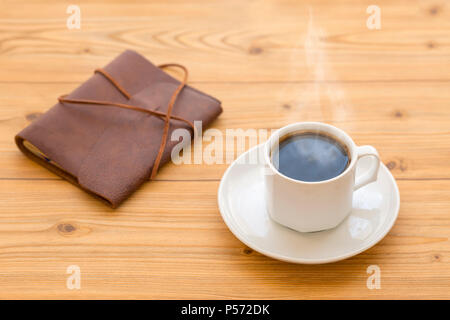 Hot coffee with steam and leather journal on the brown wooden table Stock Photo